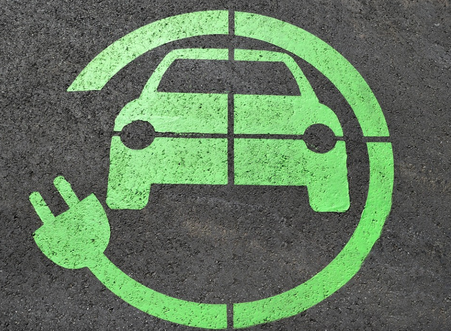 En esta imagen hay un dibujo de un ícono de auto eléctrico. Está pintado sobre el pavimento de un estacionamiento y es de color fluorescente.  